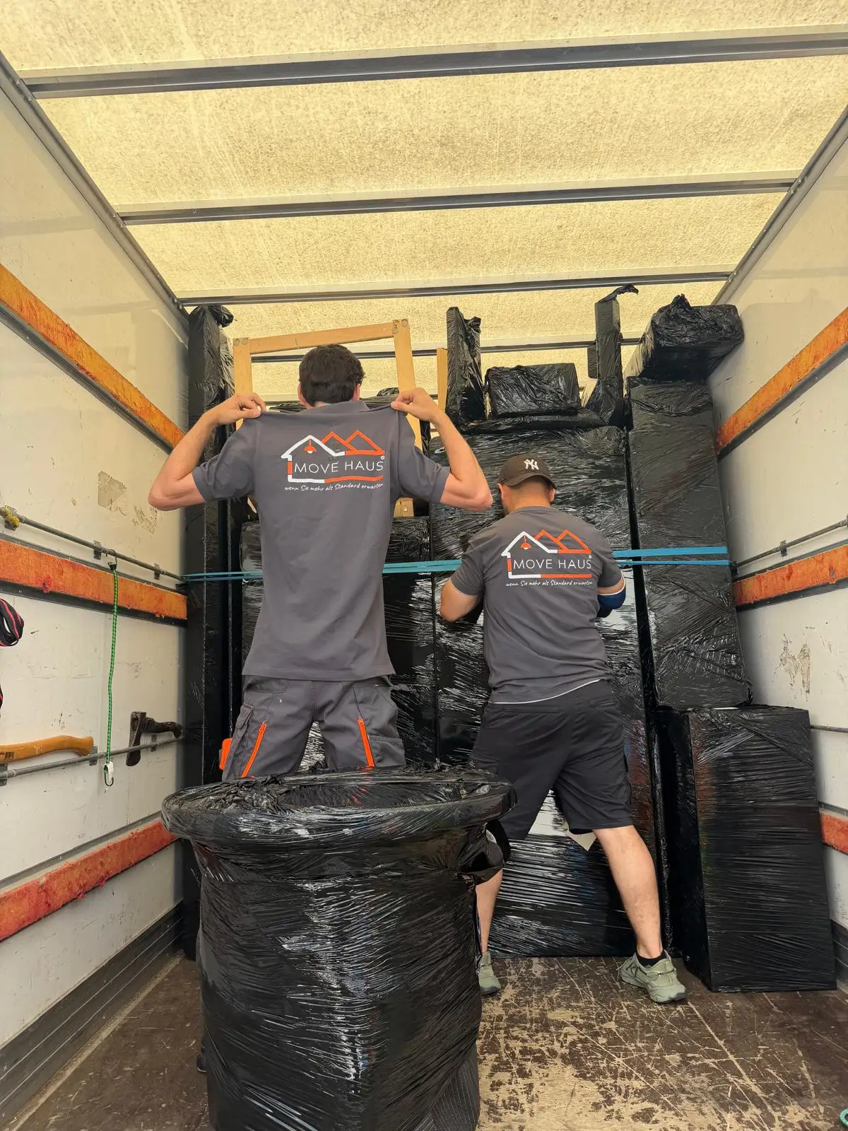 Umzugsservice Bochum – Movehaus-Mitarbeiter sichern in Folie verpackte Möbel mit Spanngurten im Umzugswagen für den Möbeltransport